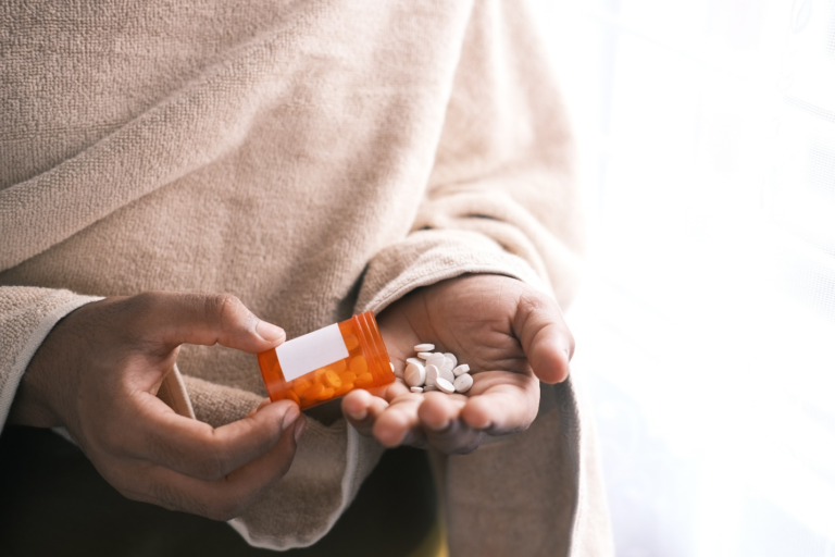 A person holding a prescription bottle and taking multiple pills.