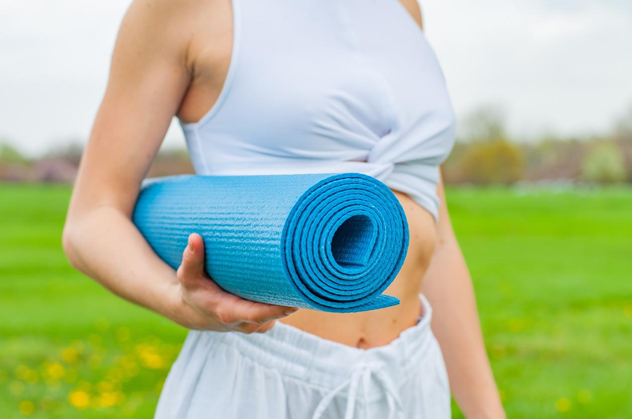 A woman in a park holding a yoga mat