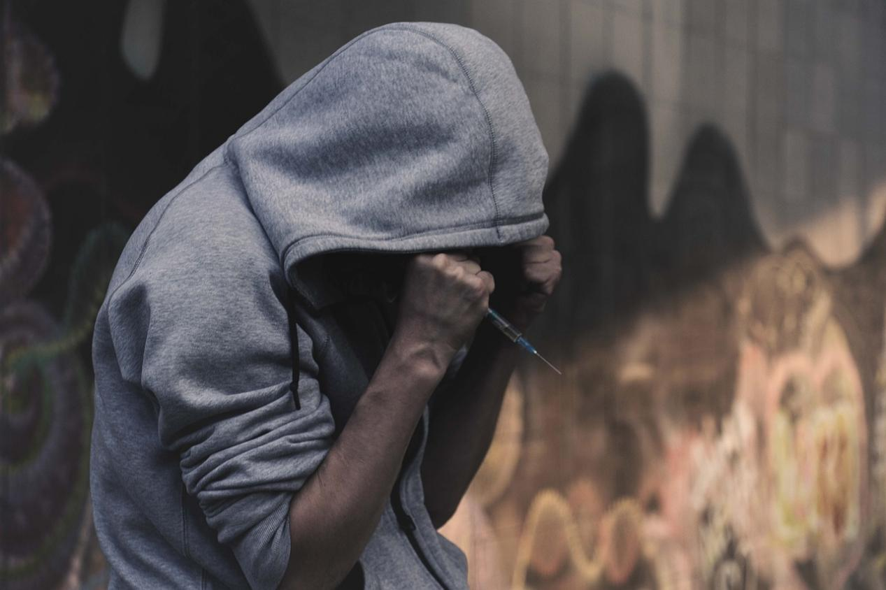 A man wearing a hoodie is holding a syringe