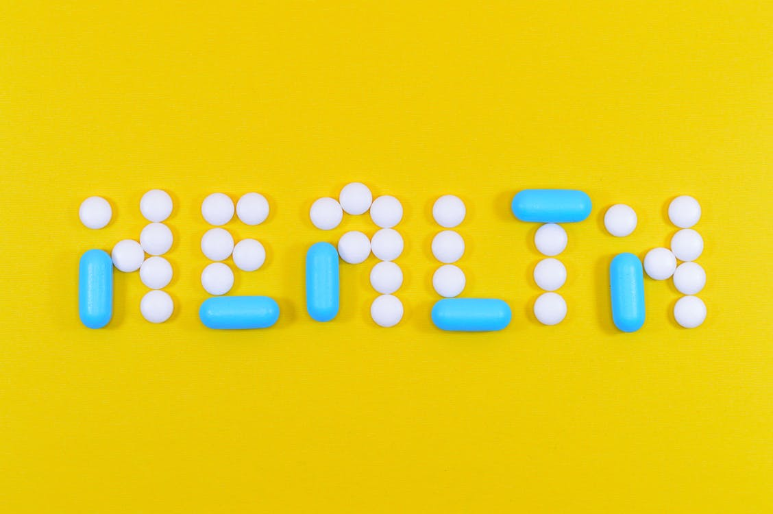 Health letter cutout on a yellow surface using pills.