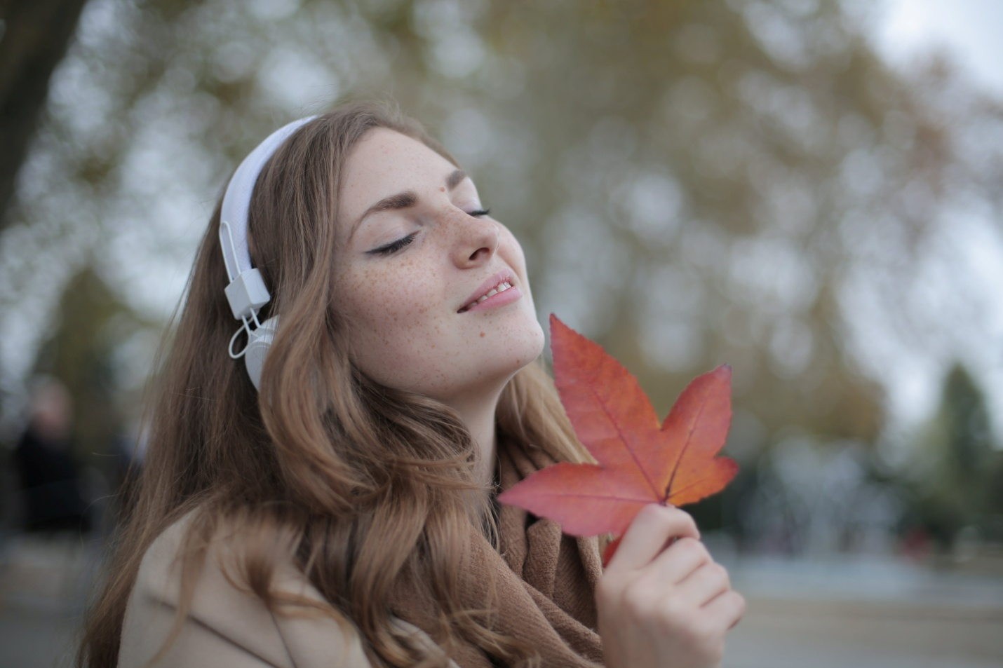 A woman wearing headphones is holding a brown leaf