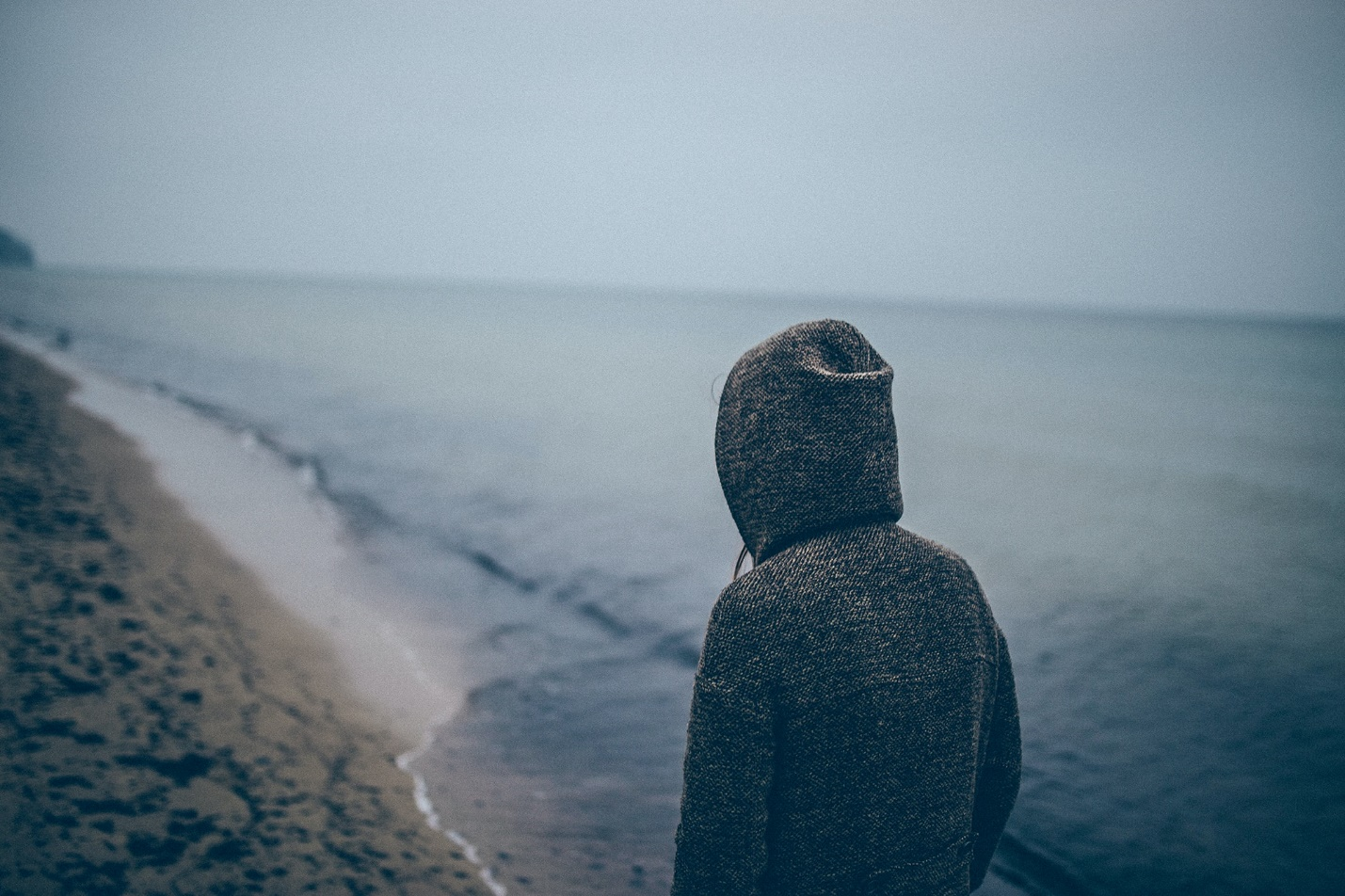 A hooded individual walks along an empty beach