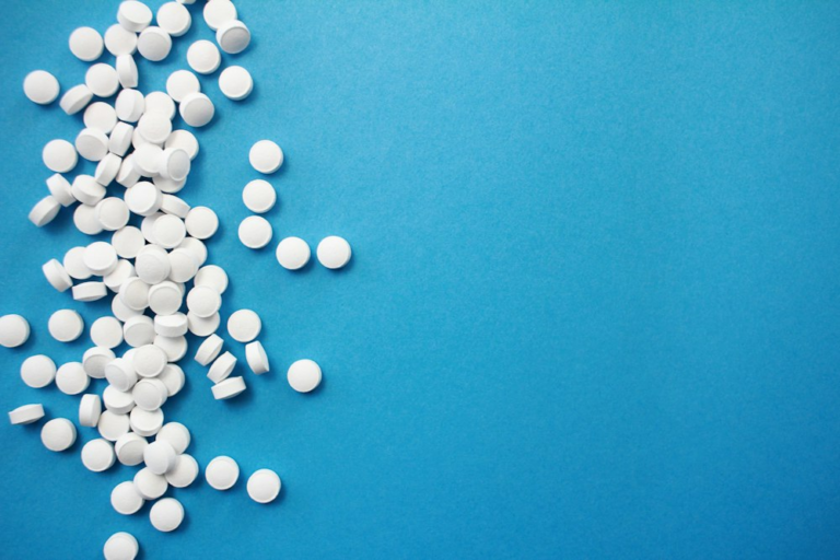 Round white pills photographed on a blue surface