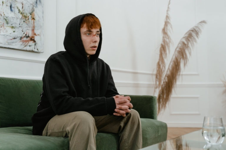 a man with nose injury in black hoodie sitting on a couch