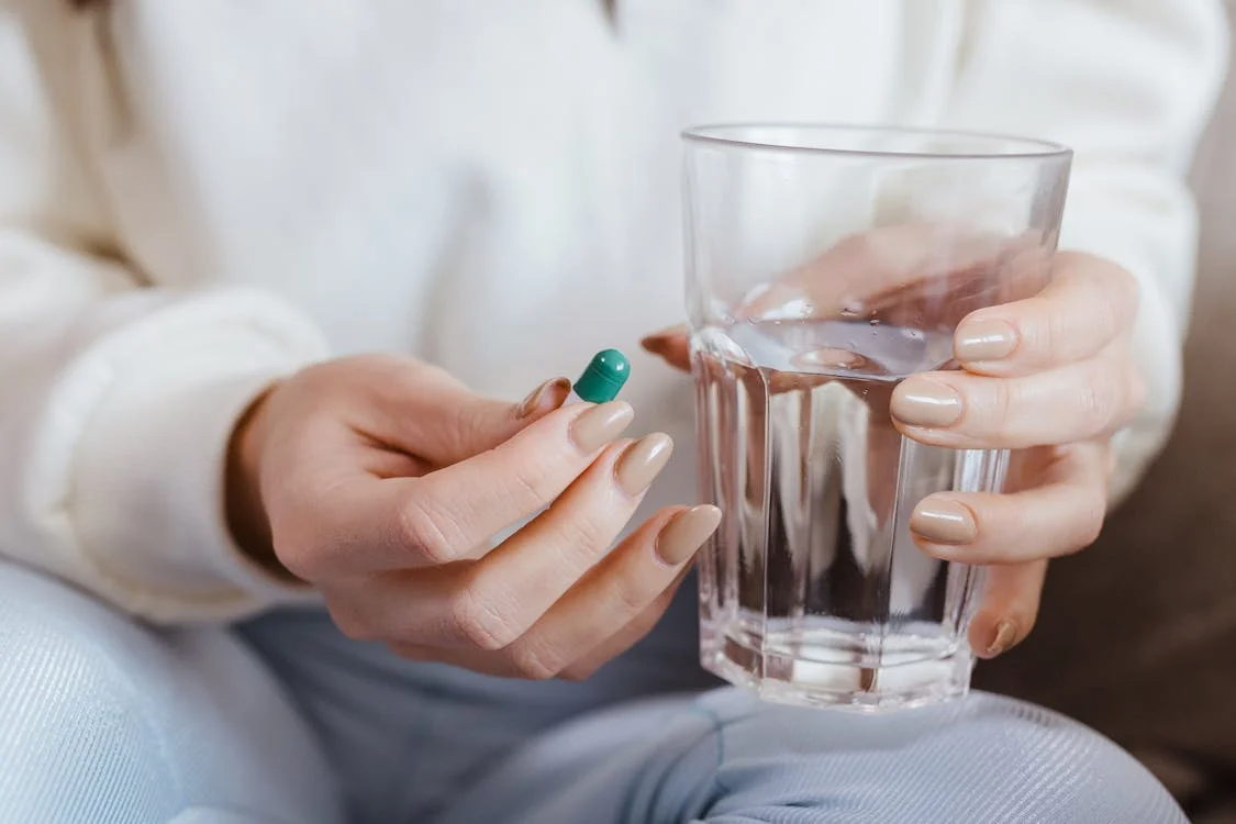 An image of a pill and a glass of water in a person’s hands