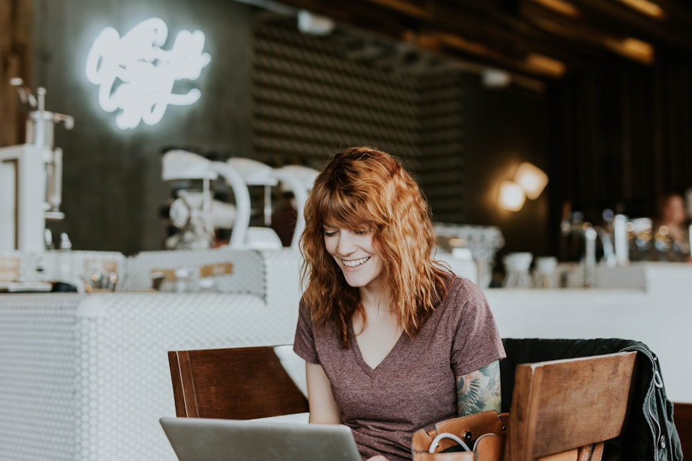 A woman smiling as she uses her laptop in a café.