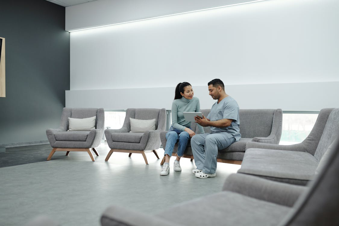 An image of a man talking to a woman while sitting on a gray couch