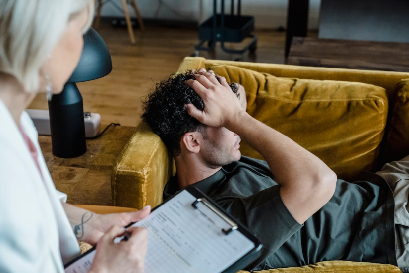 An image of a man talking to a therapist while resting on a couch and touching his head with his hands