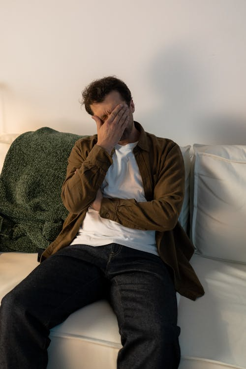 An image of a man sitting on a couch and covering his face with his hands