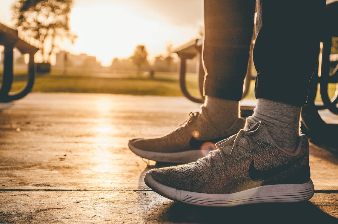 An image of a person wearing grey shoes while sitting on a bench outdoors
