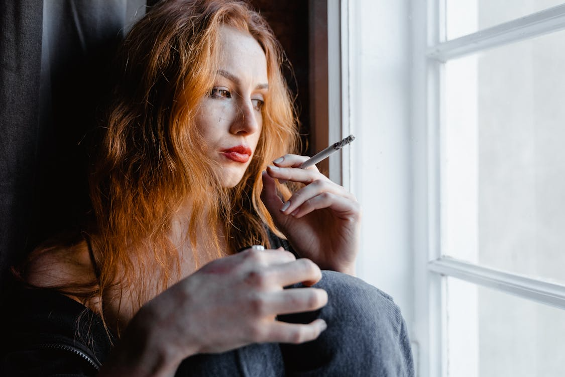 An image of a woman smoking by the window