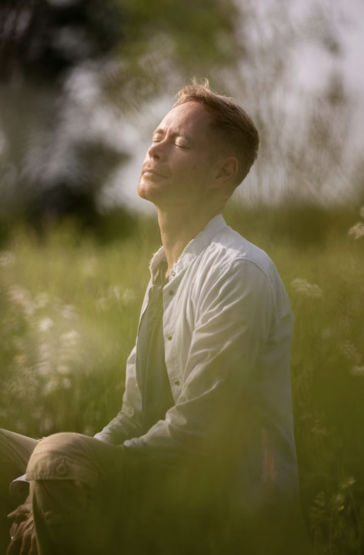 This photo shows person meditating calmly with closed eyes in morning light.