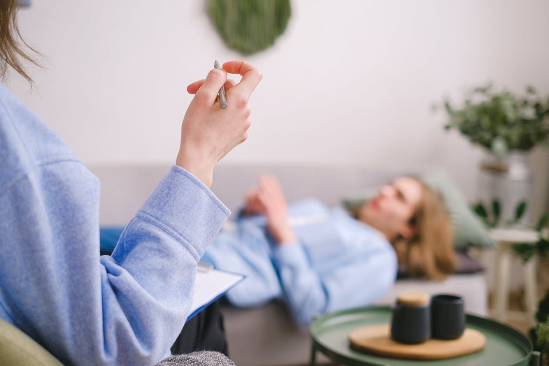 An image of an addiction therapist listening to a woman while she is lying down on a sofa