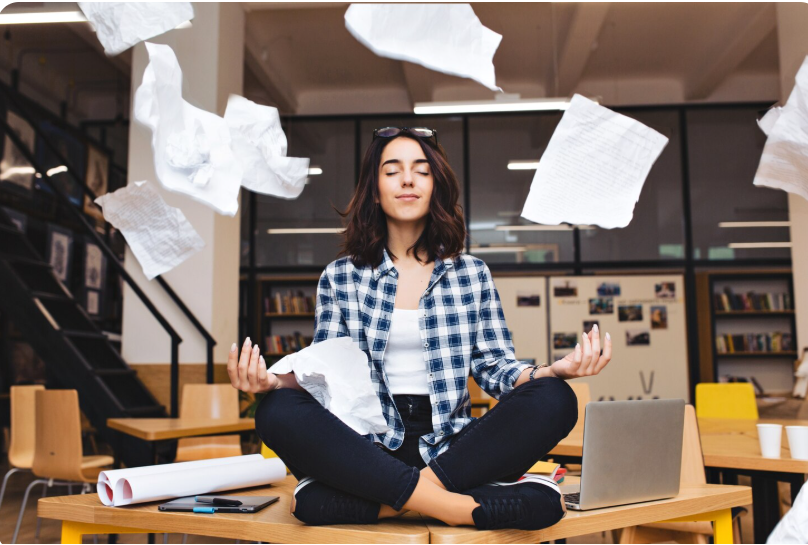 Joyful brunette woman meditating at a table with papers flying around in a relaxed, cheerful mood