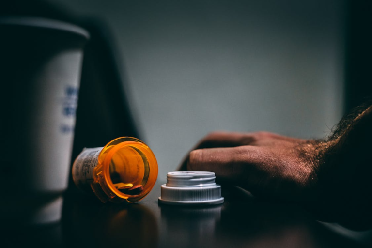 An image of an orange container of pills and a person’s hand