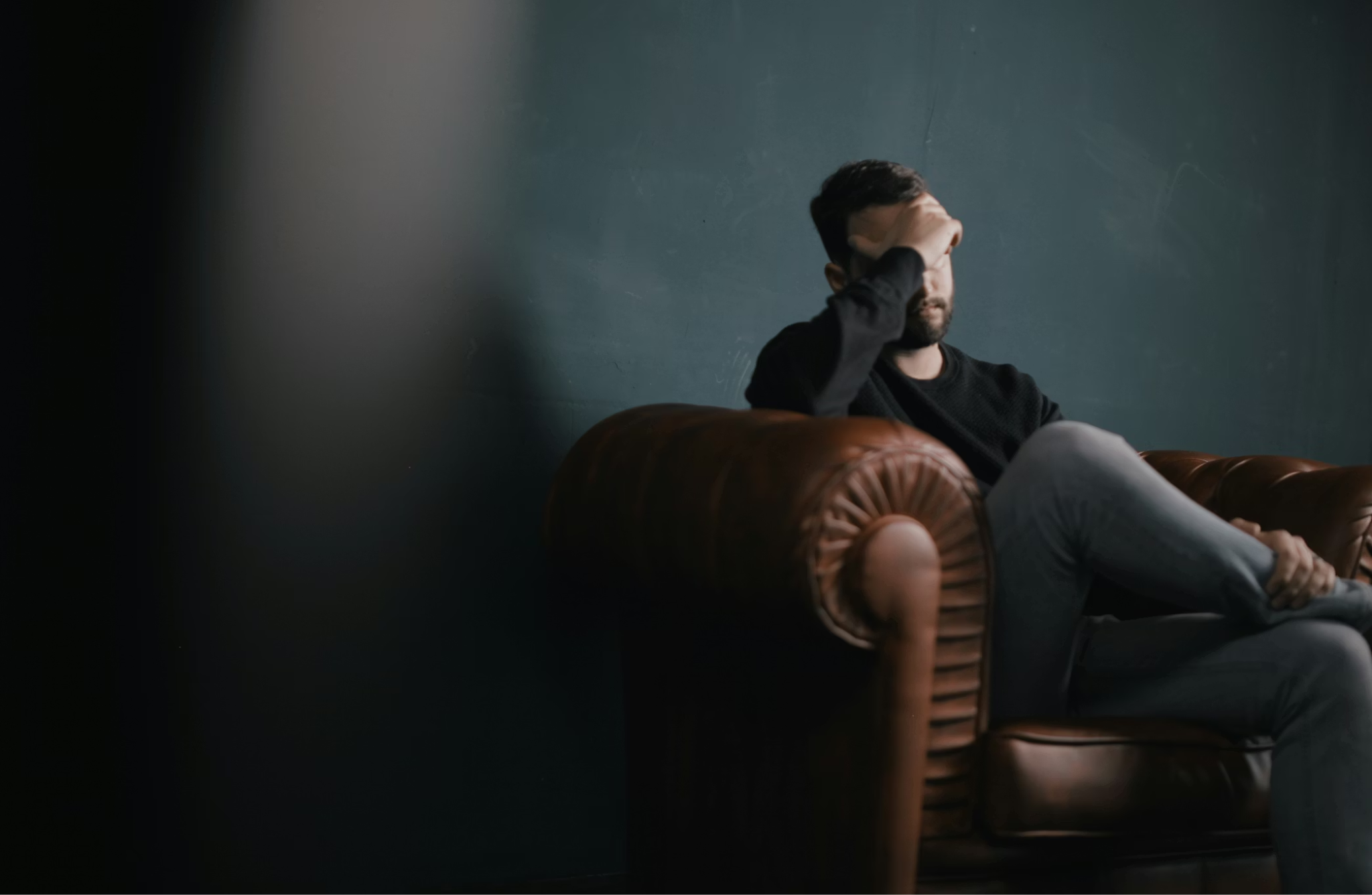 Adult man sitting on a sofa holding his head, representing emotional struggle with opioid dependence