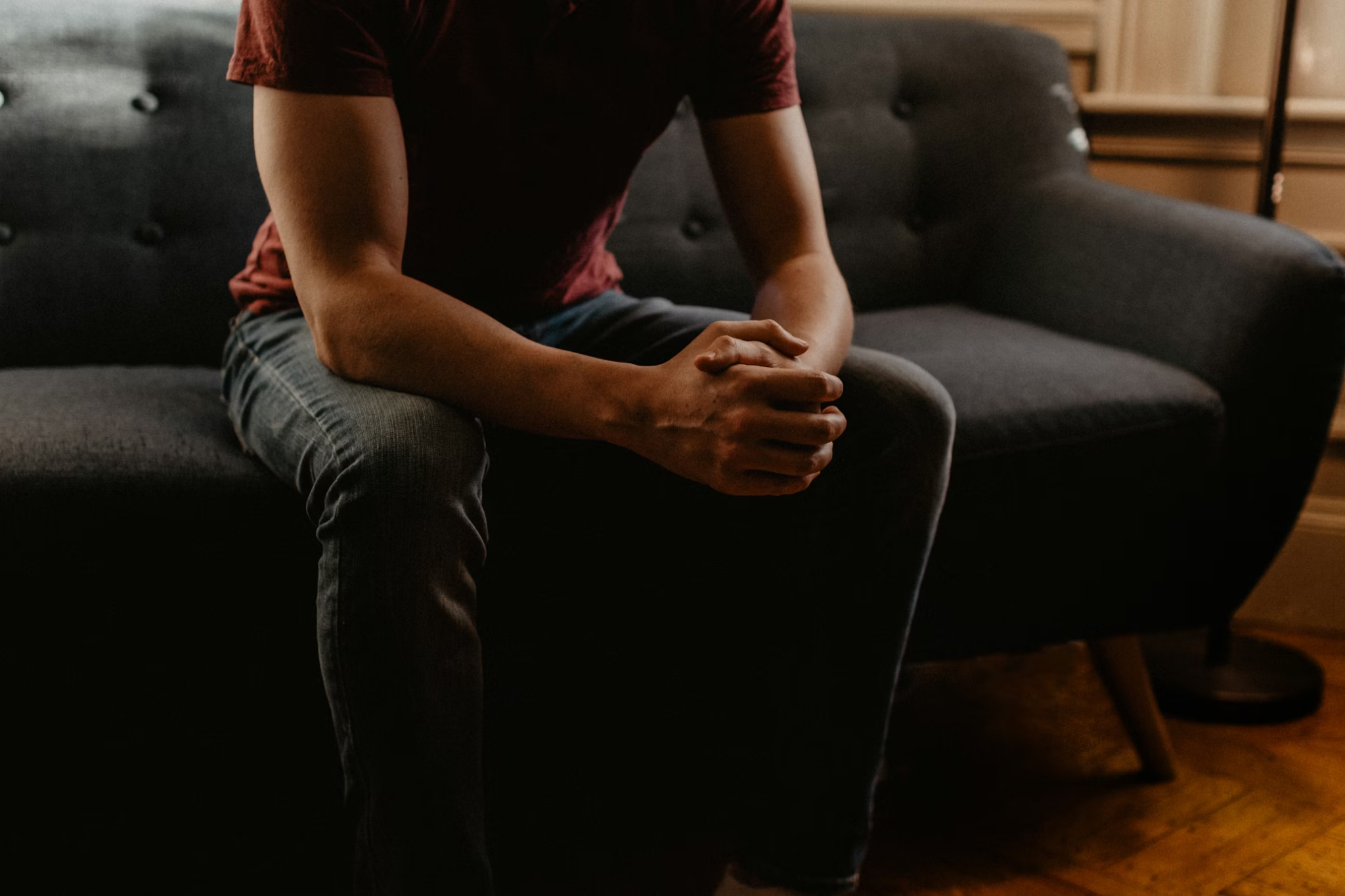 Adult man sitting on a sofa with hands clasped, reflecting during opioid recovery journey