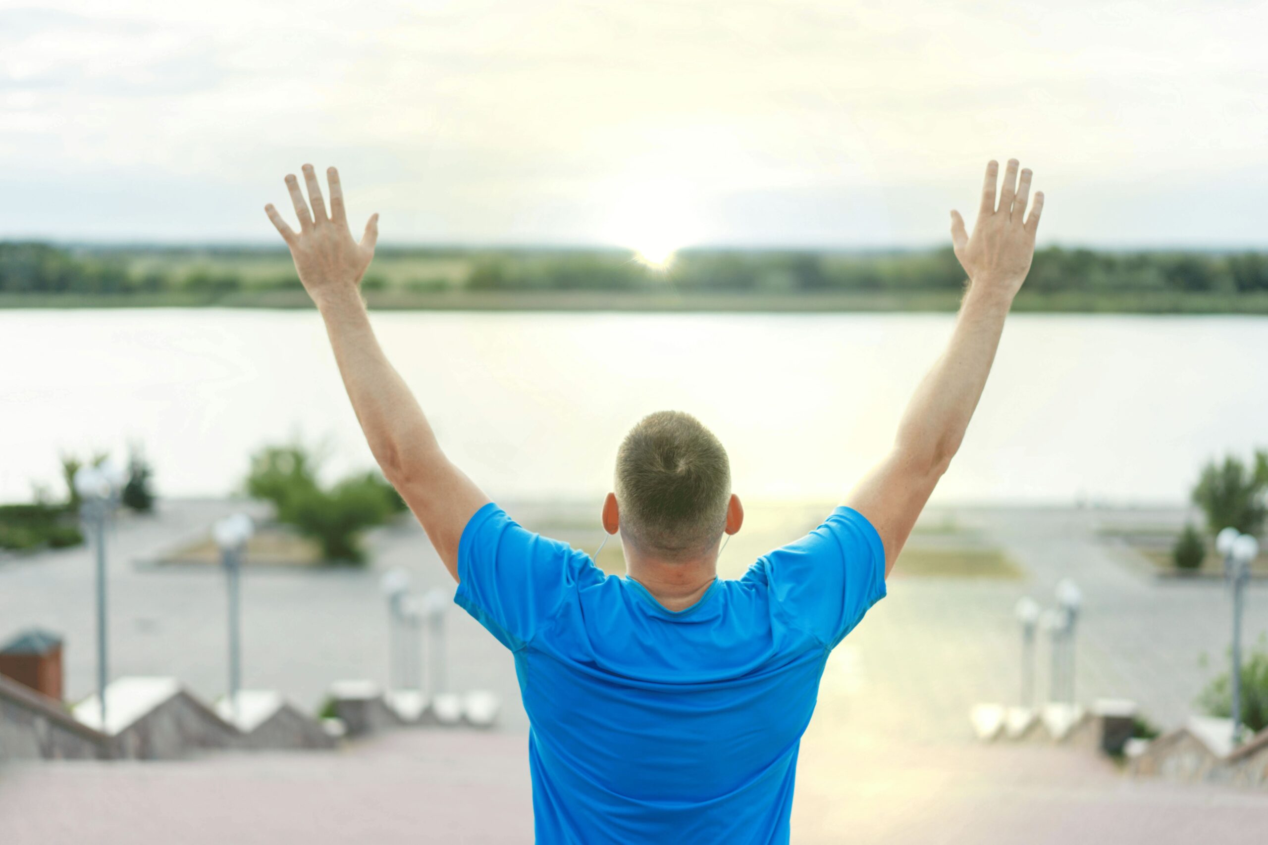 a person facing the river with hands raised in happiness