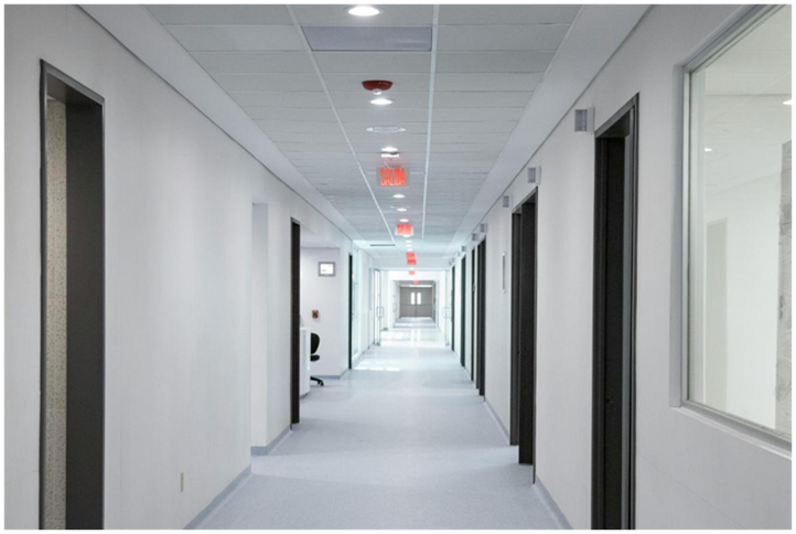 Empty white hallway in a modern medical center with doors lining the corridor and exit signs hanging from the ceiling