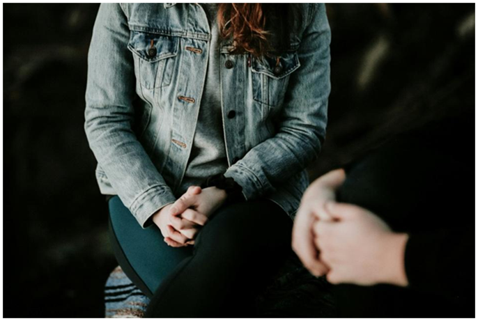 Person wearing a denim jacket sitting with hands clasped