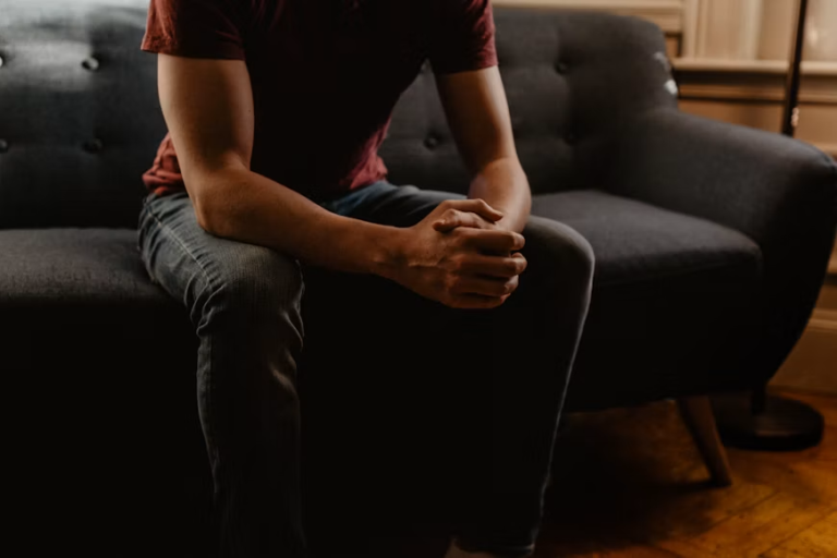 Person sitting on a sofa leaning forward with hands clasped together during a counseling session