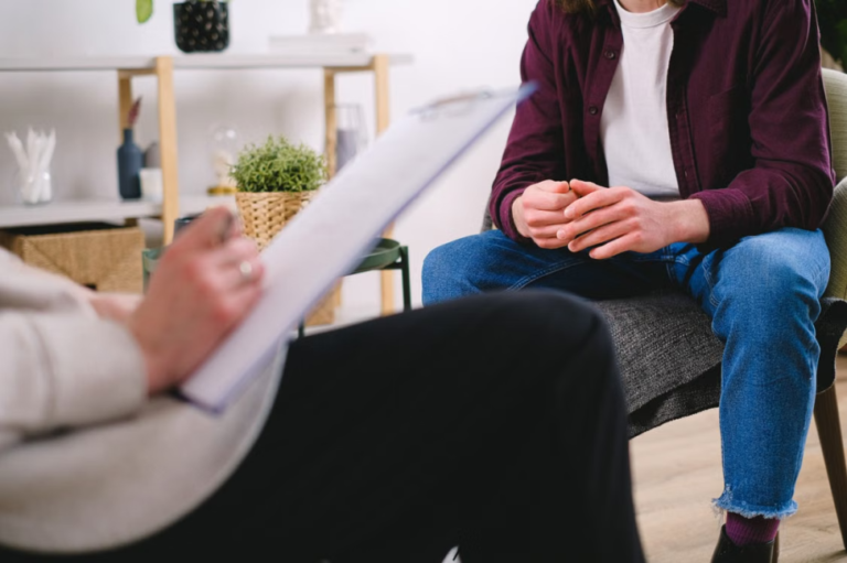 Midsection view of a therapist taking notes on a clipboard while speaking to a client sitting opposite them