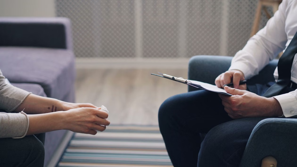 Close-up of a patient holding a tissue across from a therapist holding a clipboard during a session